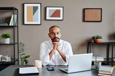 Young serious Muslim businessman in white shirt sitting by workplace